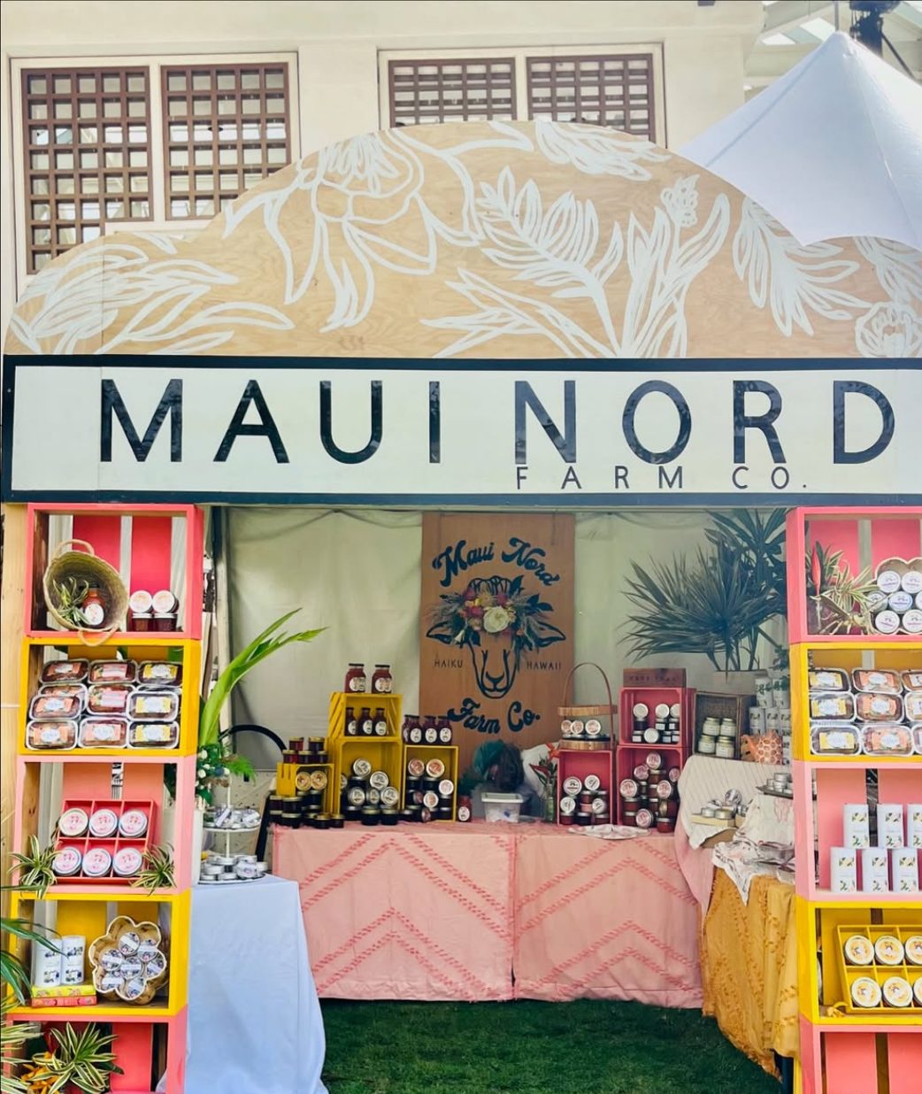 The booth arch reading Maui Nord Farm Co., with shelves of jars and bread.
