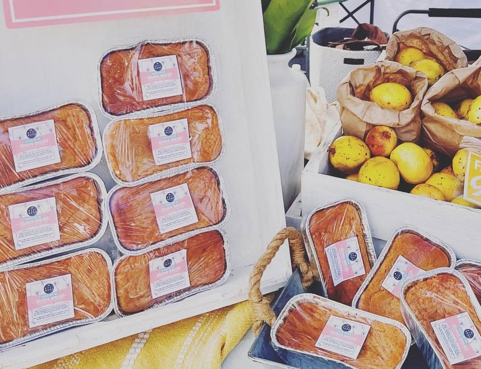 A market crate of guava bread loaves beside bags of fresh guava.
