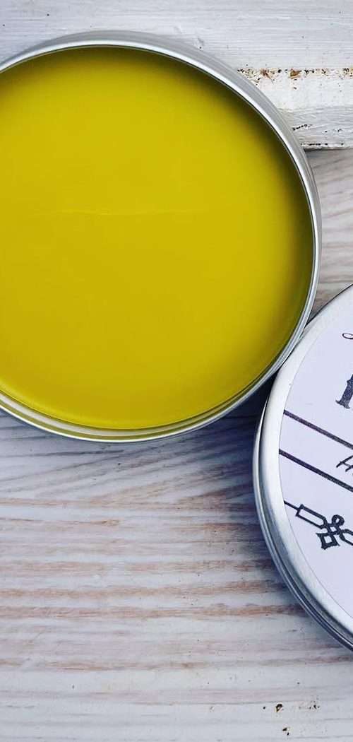 An open tin of beeswax hand salve on a whitewashed board.